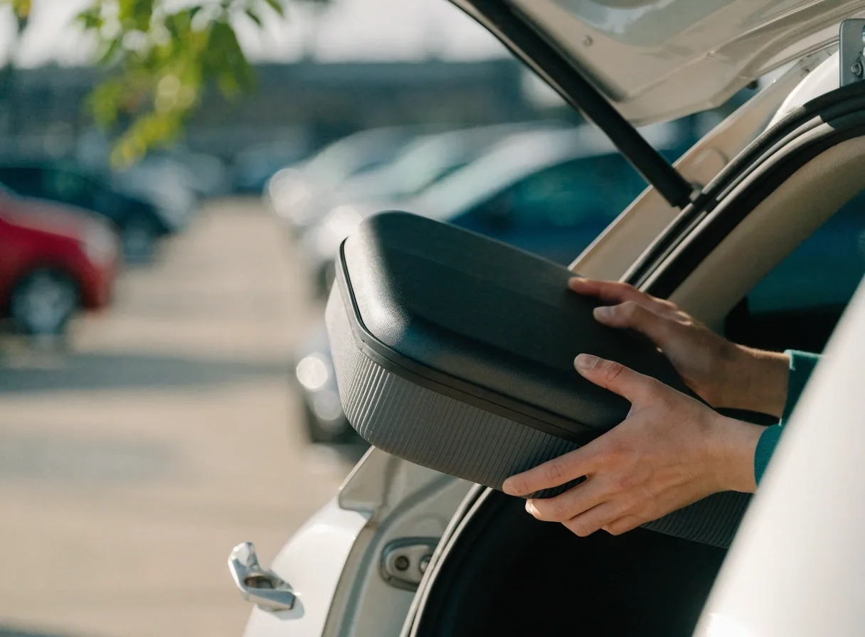 Hands loading a cabin case into a car boot at an airport car park